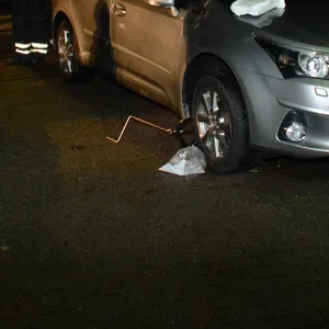 Ein silbernes Auto an der Einfahrt zu einem Parkplatz, darunter ein Wagenheber und daneben Rettungskräfte