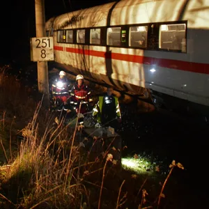 Feuerwehrleute stehen neben einem ICE an einer Bahnstrecke