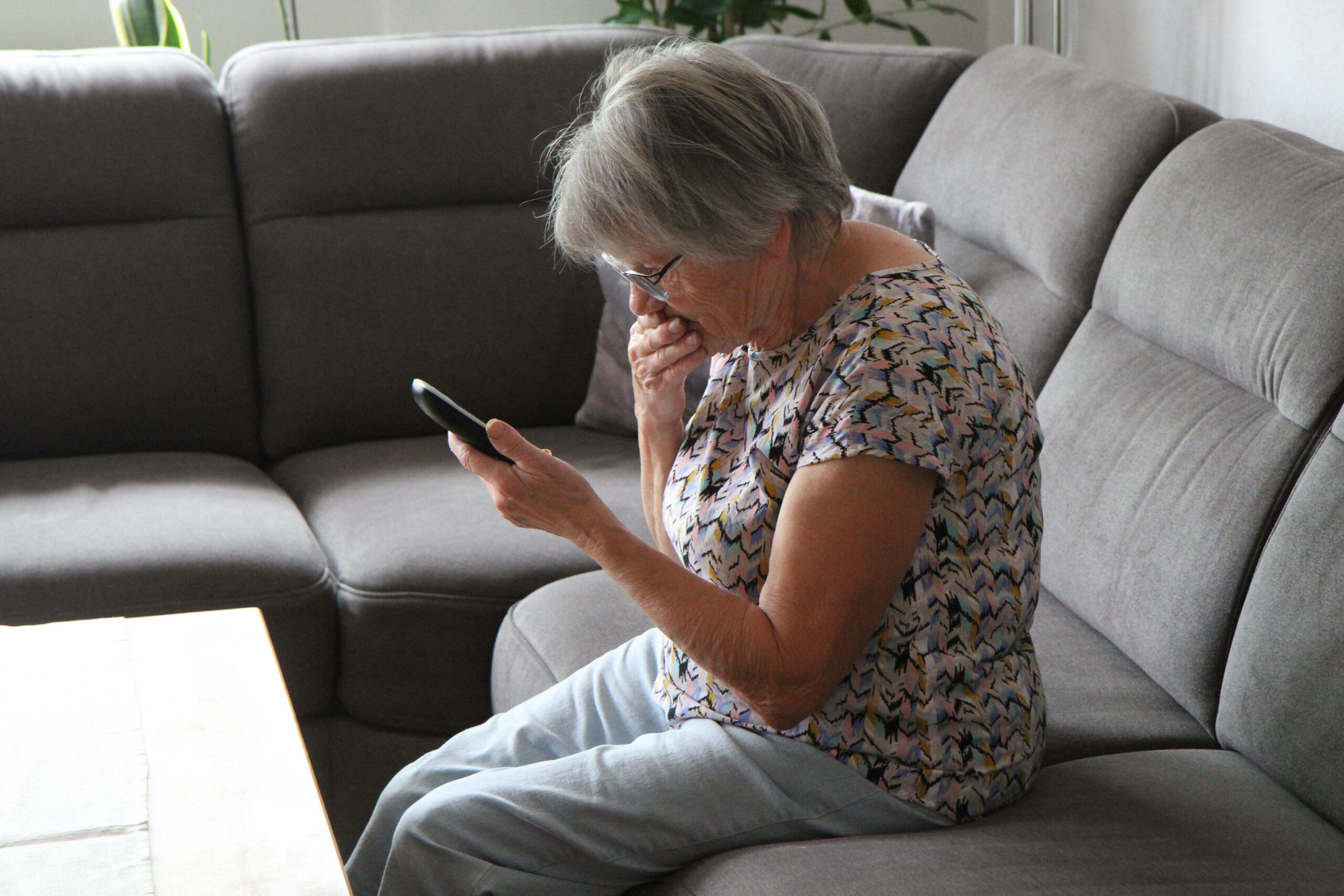 Eine ältere Frau hält ihr Telefon in der Hand, sie wirkt schockiert. (Symbolbild)