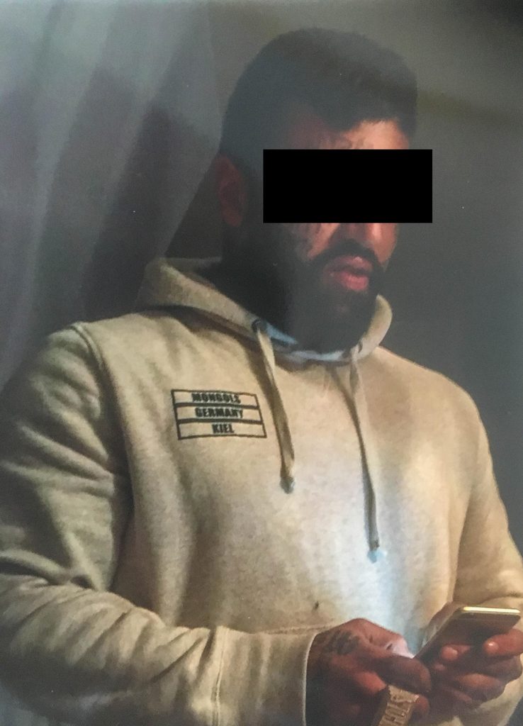 Arasch R. in einem grauen Sweatshirt, er hat einen dunklen Balknen vor den Augen.