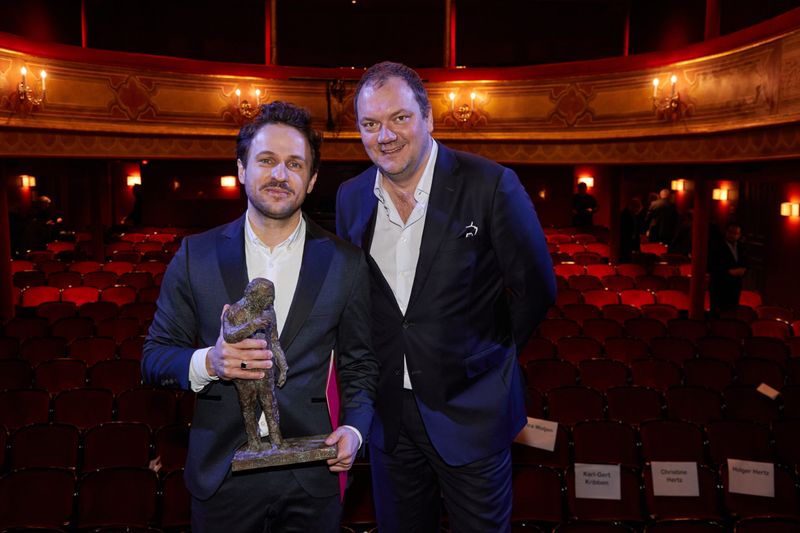 Schaad hält mit dem Preis in der Hand neben Hübner, im Hintergrund der leere Theatersaal