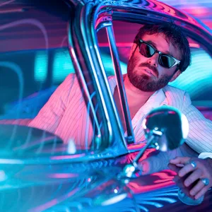 Angus Stone in Hemd und mit Sonnenbrille schaut aus dem offenen Fenster eines Cadillacs
