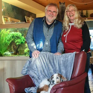Gerd (70) und Heike (68) Spiekermann mit einer der Katzen und den beiden Hunden vor dem Aquarium. Die Tiere sind essentiell für die Pflegekinder, sagen die Bereitschaftspflegeeltern.
