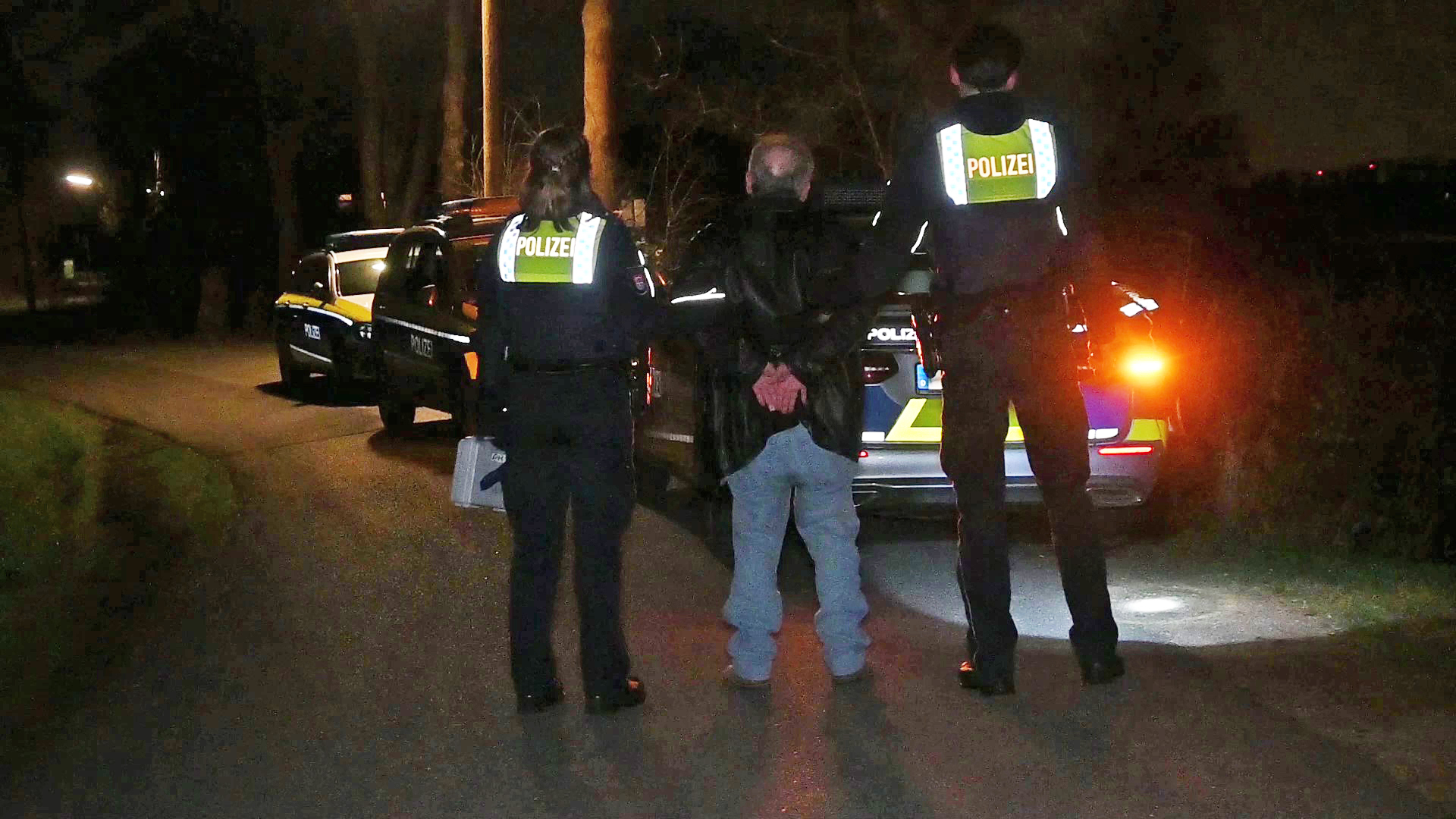 Der Mann wird von Polizisten in Handschellen zum Streifenwagen begleitet.