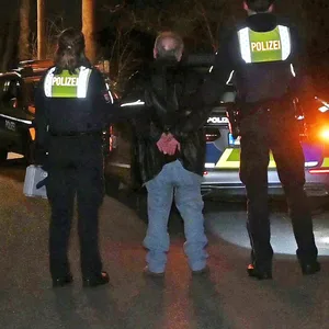 Der Mann wird von Polizisten in Handschellen zum Streifenwagen begleitet.