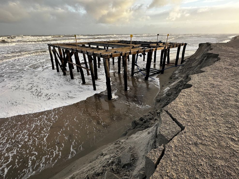 Wellen umspülen bei stürmischem Wetter am Strandabschnitt „Weiße Düne“ ein Holzgerüst für Umkleidekabinen und die Badeaufsicht.