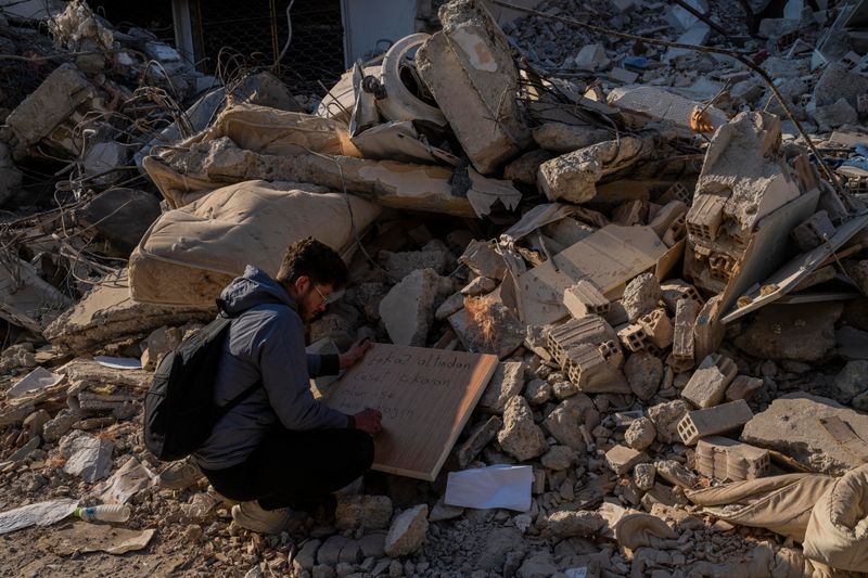 Ein junger Mann kniet vor den Trümmern und schreibt auf ein Stück Holz.