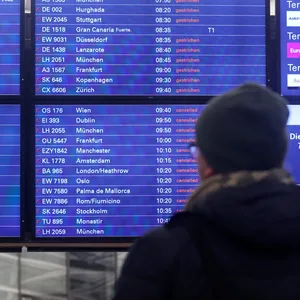 Ein Mann blickt am Flughafen Hamburg auf eine Anzeigentafel, auf der zahlreiche gestrichene Flüge angezeigt werden.