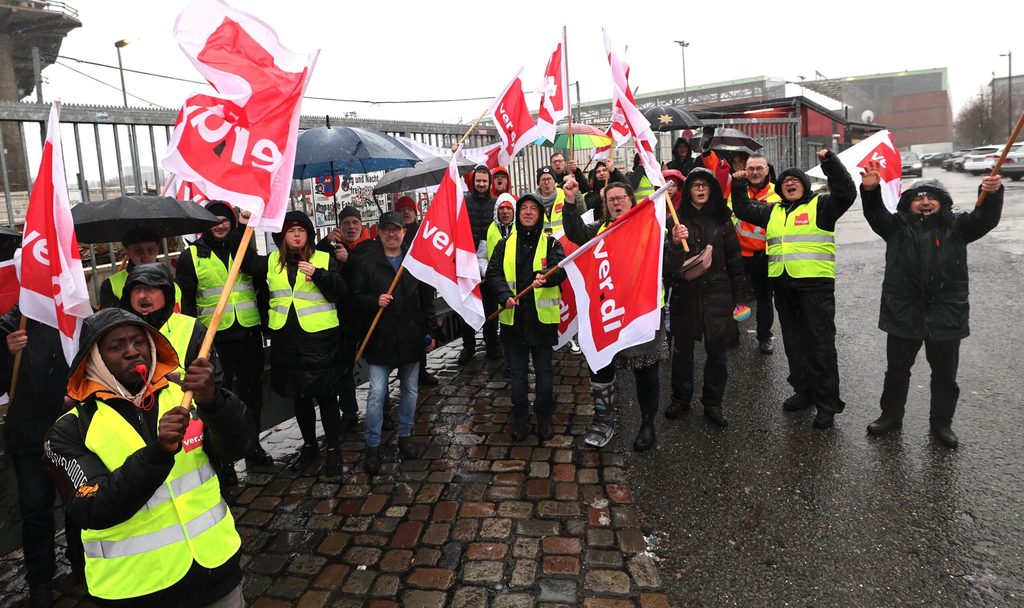 Beschäftigte von Recyclinghöfen und Verdi-Mitglieder stehen nach einer Abschlusskundgebung zu ihrem Warnstreik vor den geschlossenen Toren des Recyclinghofs St. Pauli.