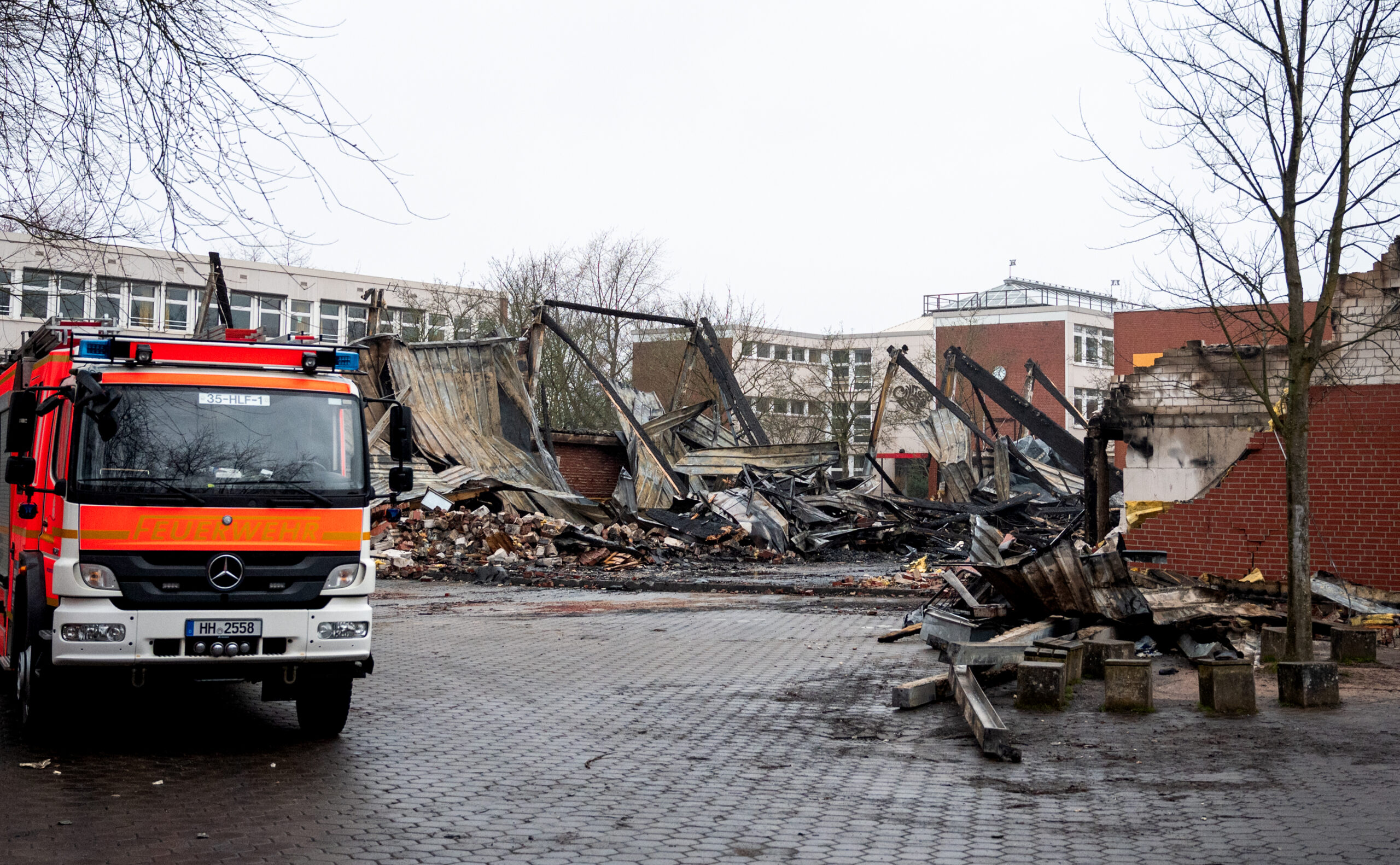 Ein Fahrzeug der Feuerwehr steht vor den Resten der abgebrannten Turnhalle in Finkenwerder.