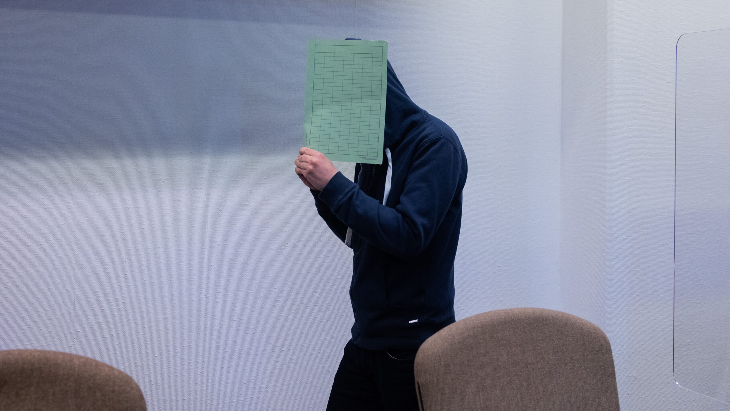 Der Angeklagte im Missbrauchskomplex Wermelskirchen hält sich im Gerichtssaal eine Mappe vor das Gesicht.