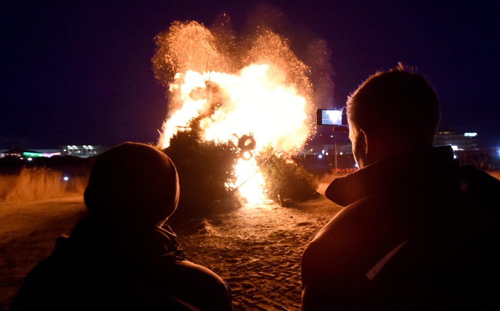 Besucher stehen am Strand von St. Peter-Ording (Schleswig-Holstein) vor dem Biikefeuer.