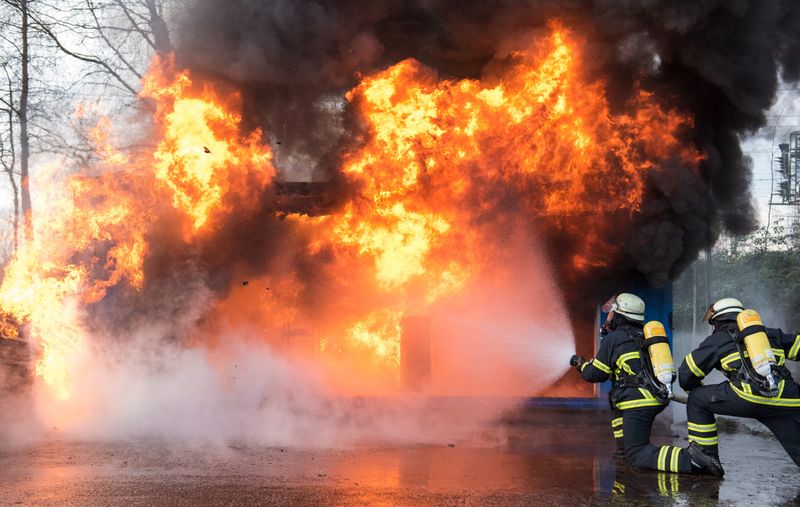 Feuerwehrleute löschen während einer Vorführung ein nachgebautes Wohnzimmer, in dem ein Tannenbaum in Brand geraten ist.