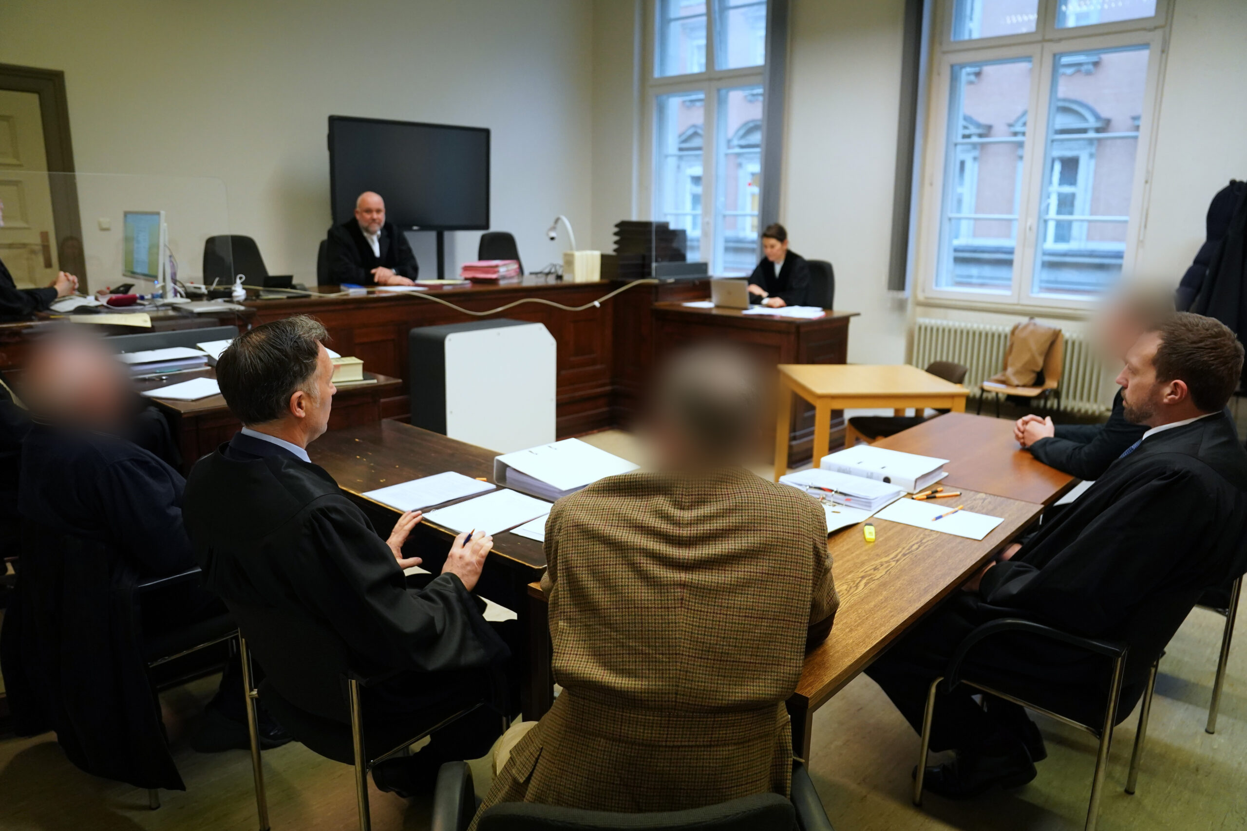Die Angeklagten (links, mittig, und hinten rechts) sitzen mit ihren Anwälten zu Beginn des Prozesstages im Sitzungssaal.
