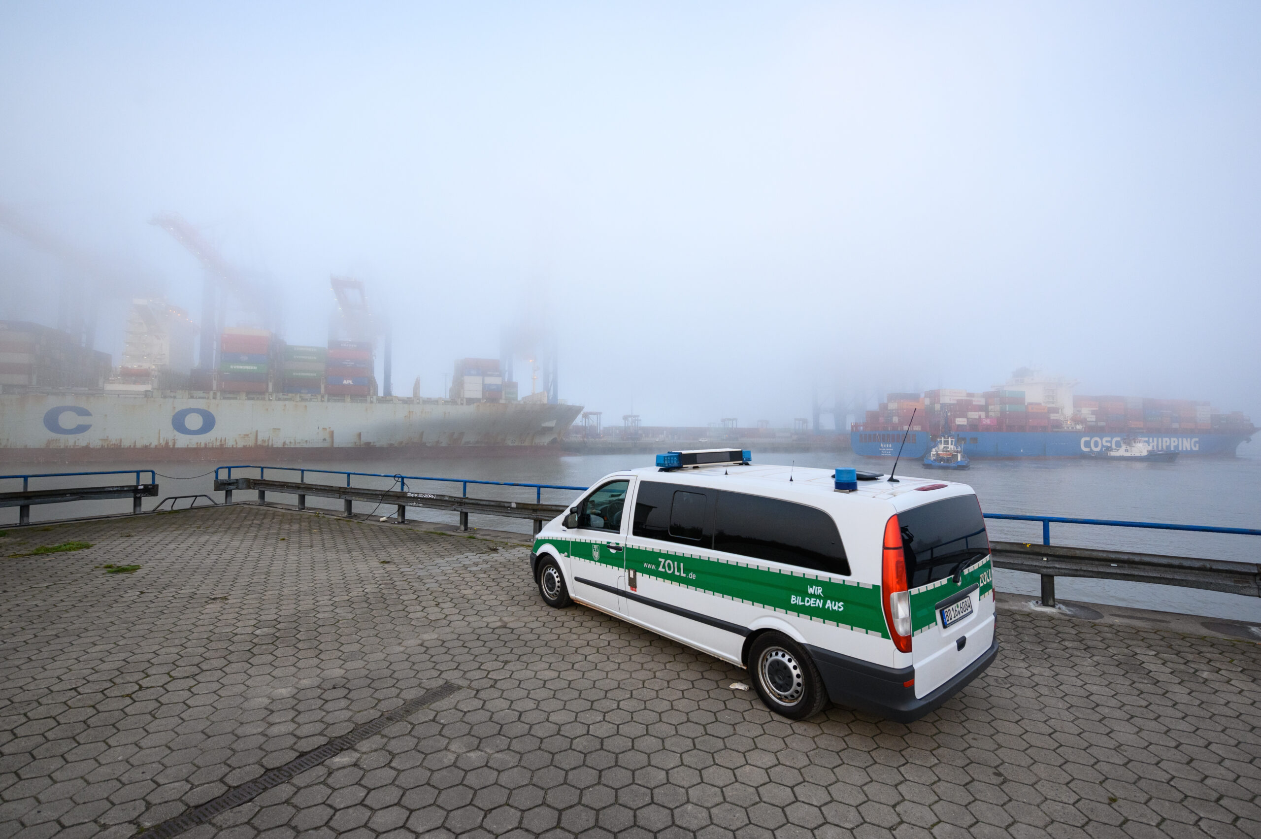 Ein Einsatzfahrzeug des Zolls steht gegenüber dem im Nebel liegenden Containerterminal Tollerort.