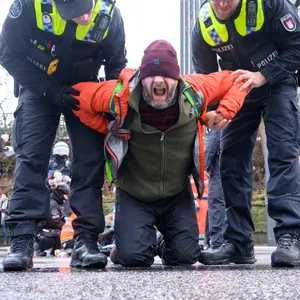Schreien fürs Klima: Zwei Polizisten halten einen Aktivisten (M.) auf der Straße fest. Er hatte sich auf die viel befahrene Edmund-Siemers-Allee am Dammtorbahnhof geklebt.