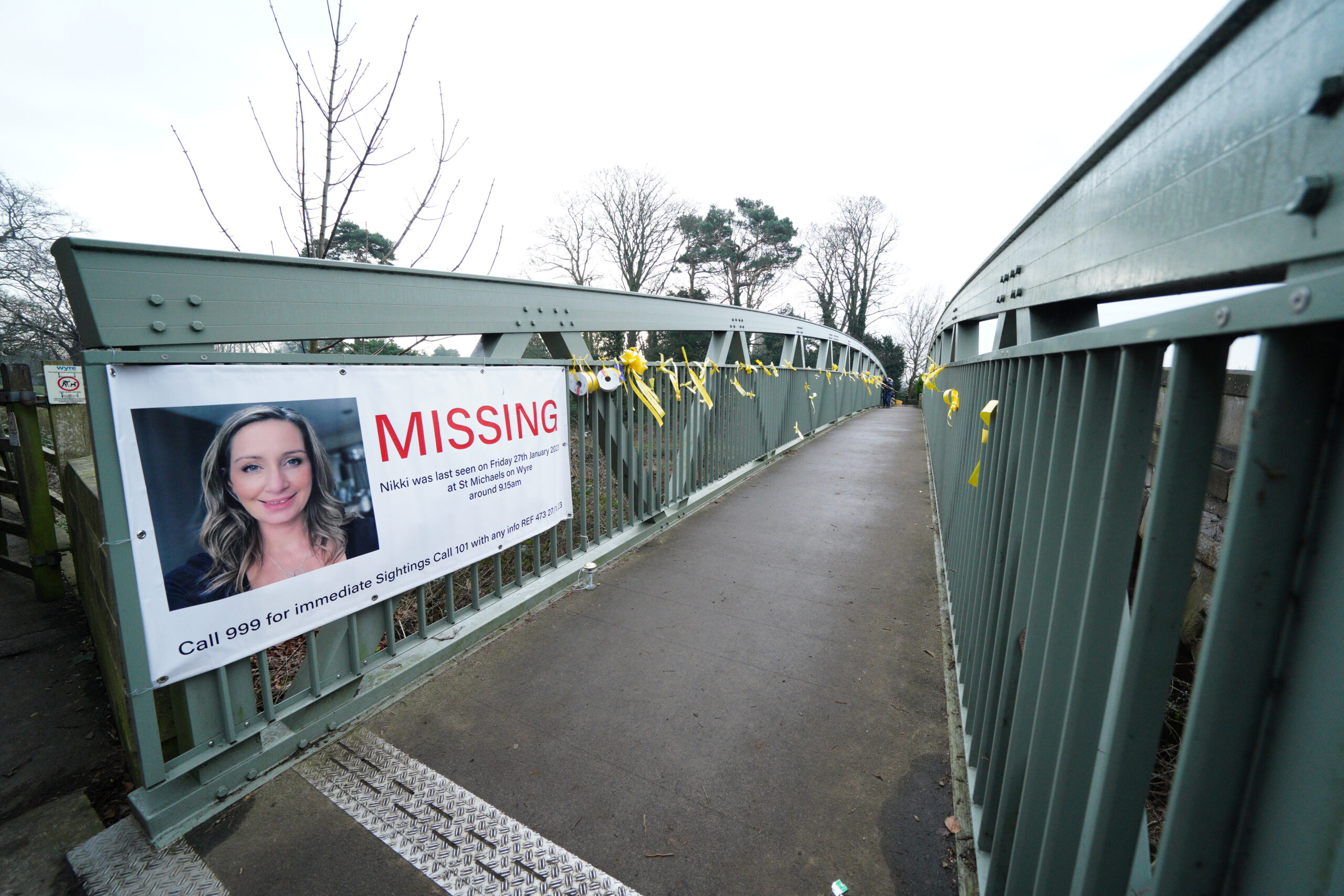 Ein Plakat mit einem Vermisstenaufruf für Nicola Bulley und gelbe Bänder mit Hoffnungsbotschaften, die an einer Brücke über den Fluss Wyre befestigt sind