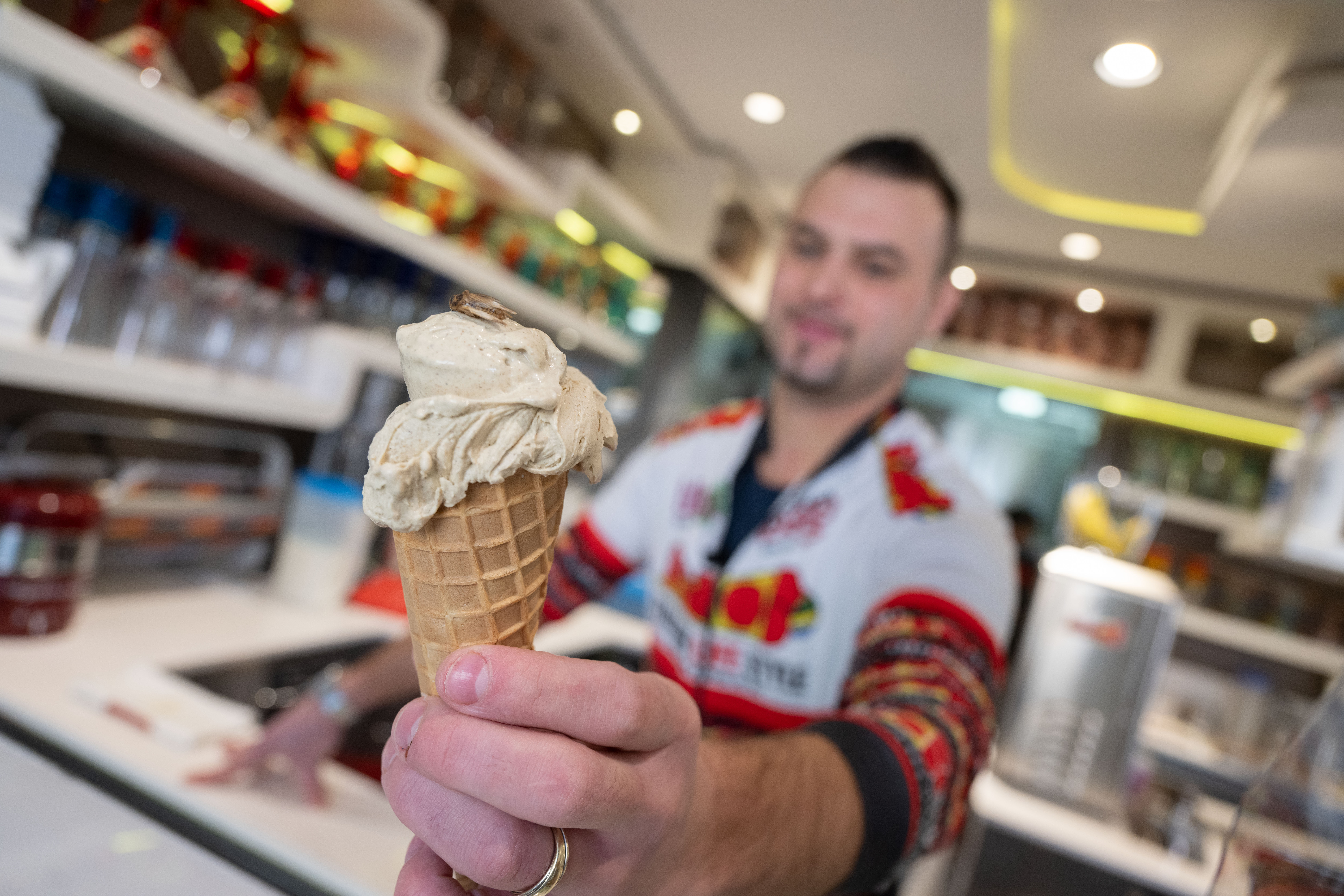 Thomas Micolino, Inhaber des Eiscafé Rino, zeigt ein Eis, das zum Teil aus Grillenmehl besteht und auf dem ein getrocknetes Heimchen sitzt