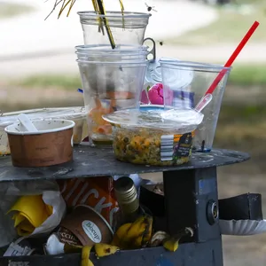 Ein übervoller Mülleimer mit Partymüll aus Plastik steht in einem Park. (Symbolbild)