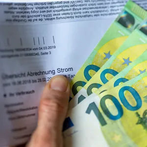 Hand mit Geld und Stromrechnung