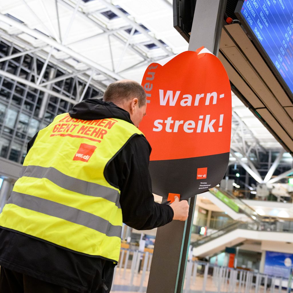 Ein Verdi-Vertreter klebt ein Plakat mit der Aufschrift „Warnstreik!“ die Anzeigetafel im leeren Terminal 2 am Hamburg Airport.