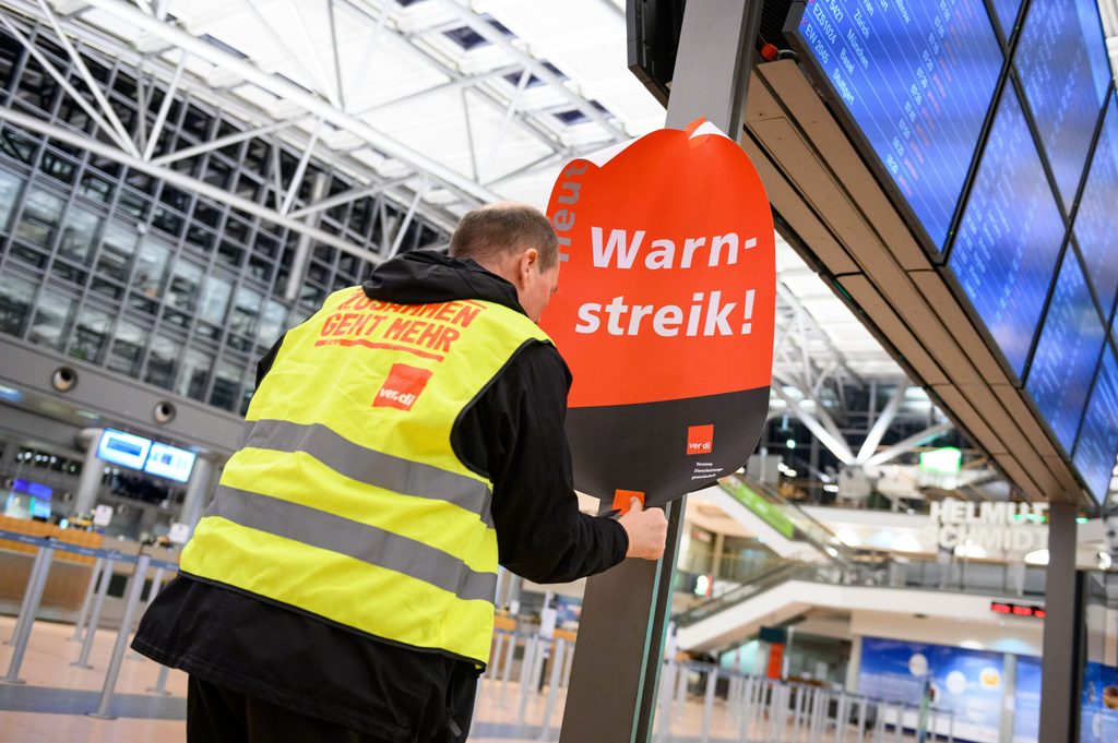 Ein Verdi-Vertreter klebt ein Plakat mit der Aufschrift „Warnstreik!“ die Anzeigetafel im leeren Terminal 2 am Hamburg Airport.