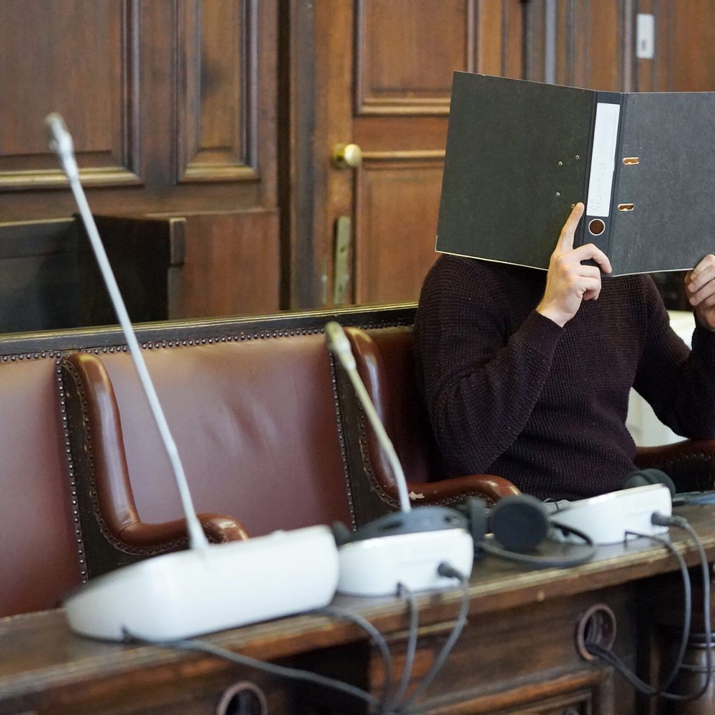 Der angeklagte Messerstecher verbirgt im Sitzungssaal sein Gesicht