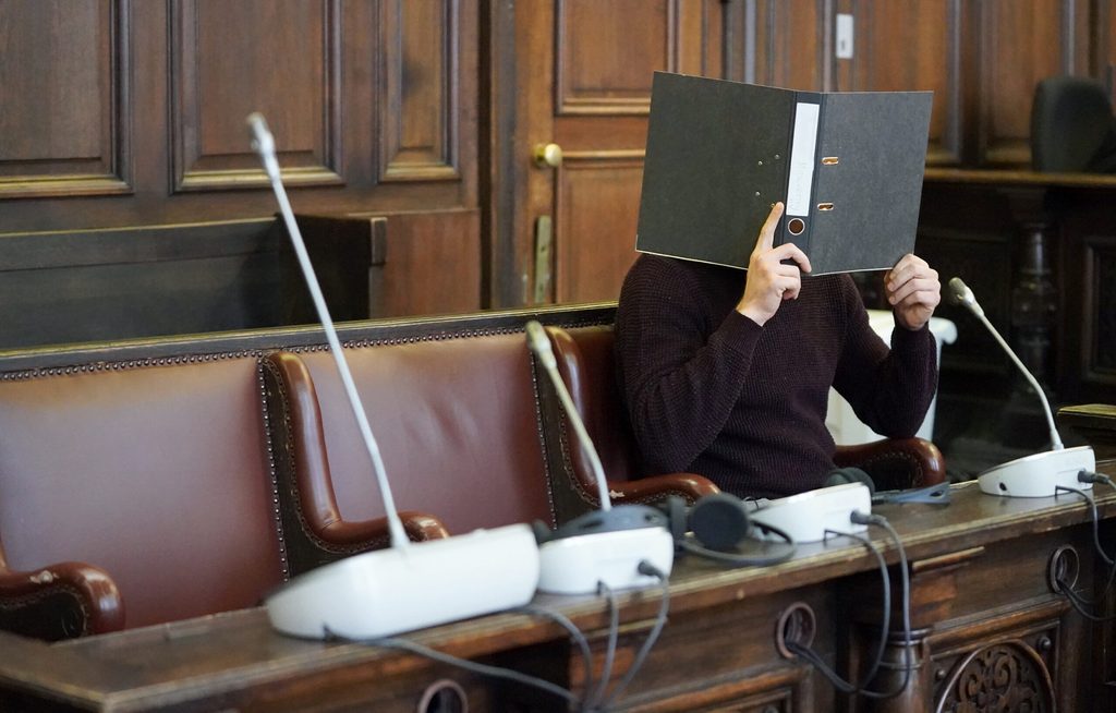 Der angeklagte Messerstecher verbirgt im Sitzungssaal sein Gesicht