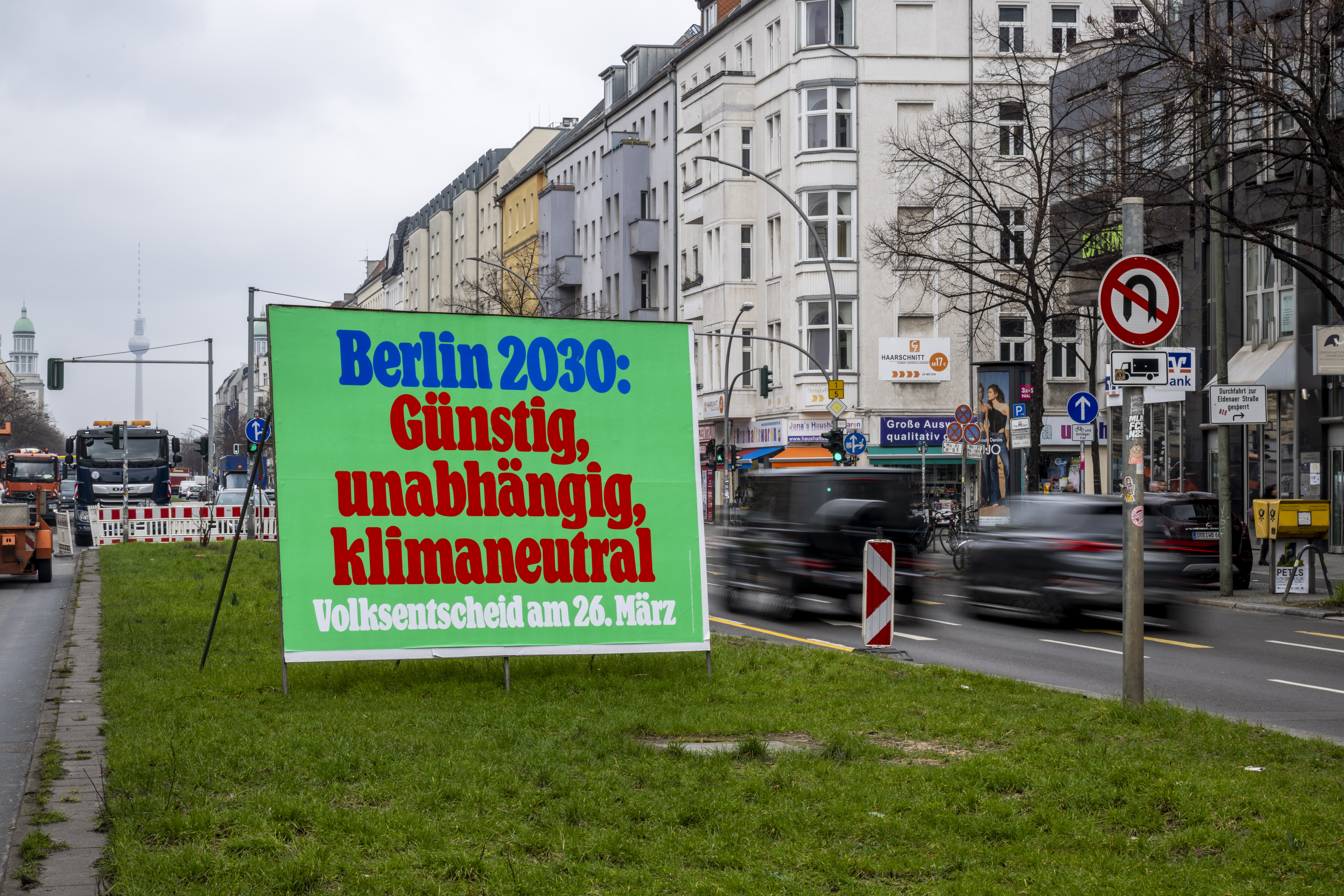Ein Plakat mit der Aufschrift „Berlin 2030: Günstig, unabhängig, klimaneutral - Volksentscheid am 26. März“ steht auf der Frankfurter Allee