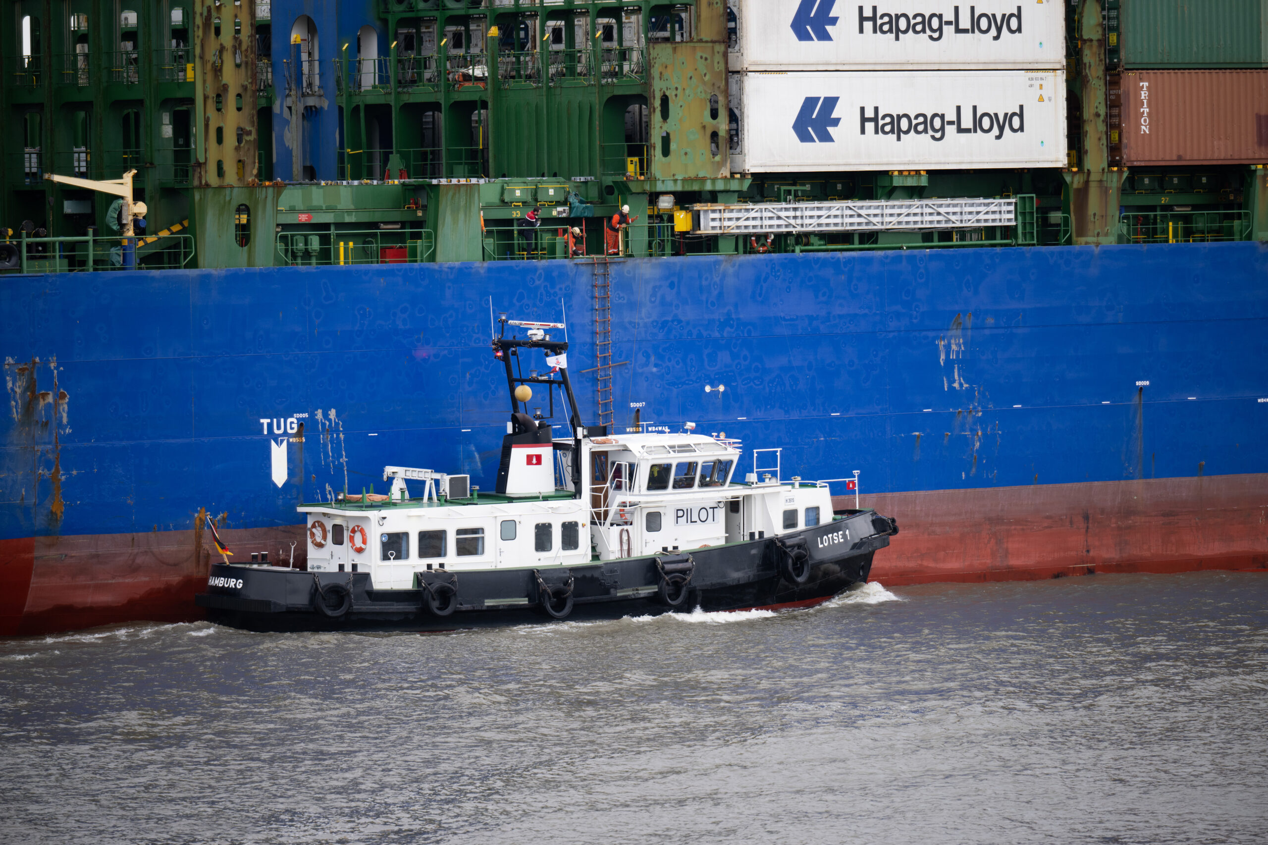 Ein Lotsenboot fährt neben einem Containerschiff, nachdem es einen Lotsen an Bord genommen hat.