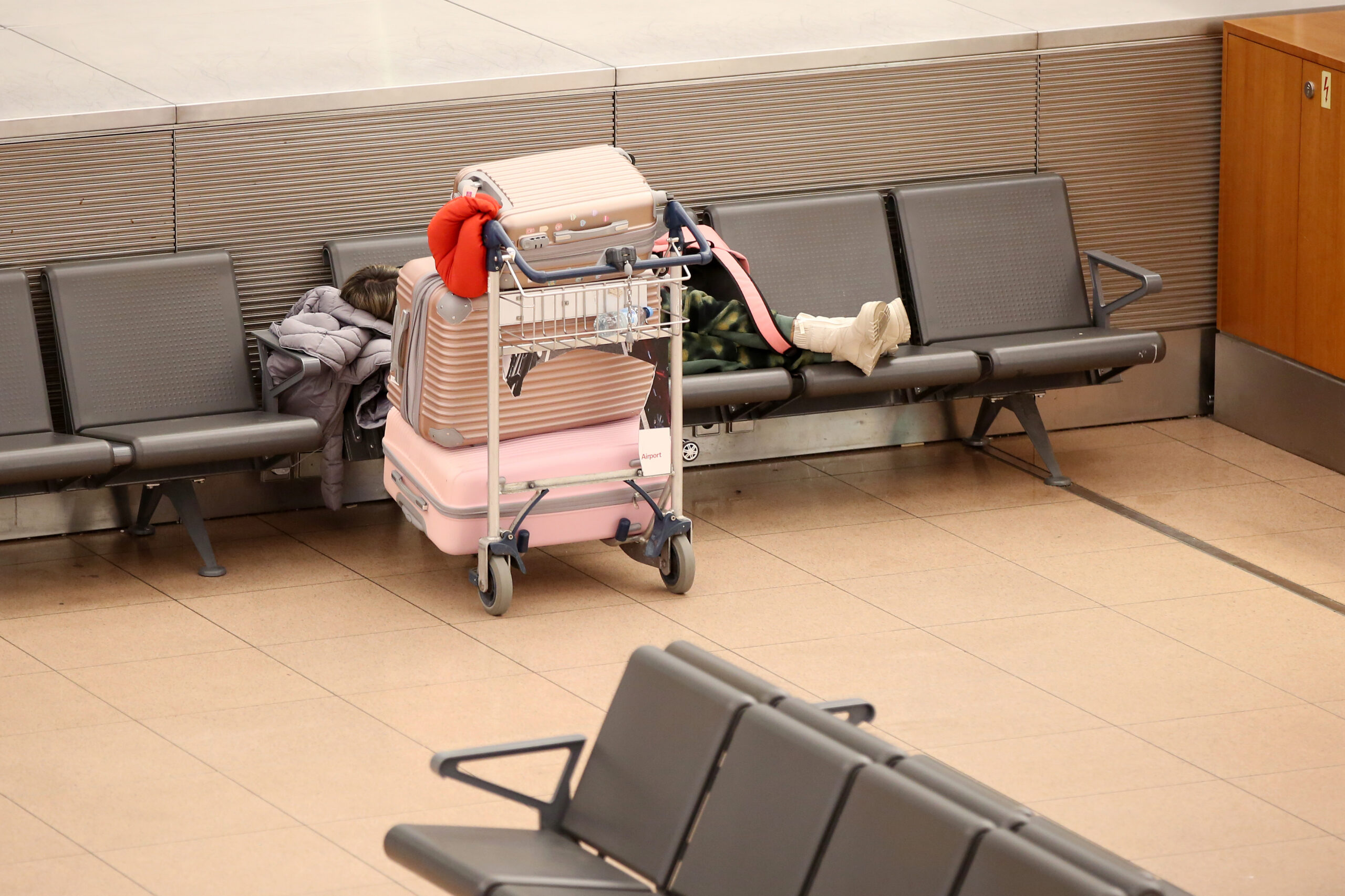Eine Reisende liegt neben ihren Koffern auf einer Bank im ansonsten menschenleeren Terminal 1 im Flughafen Hamburg