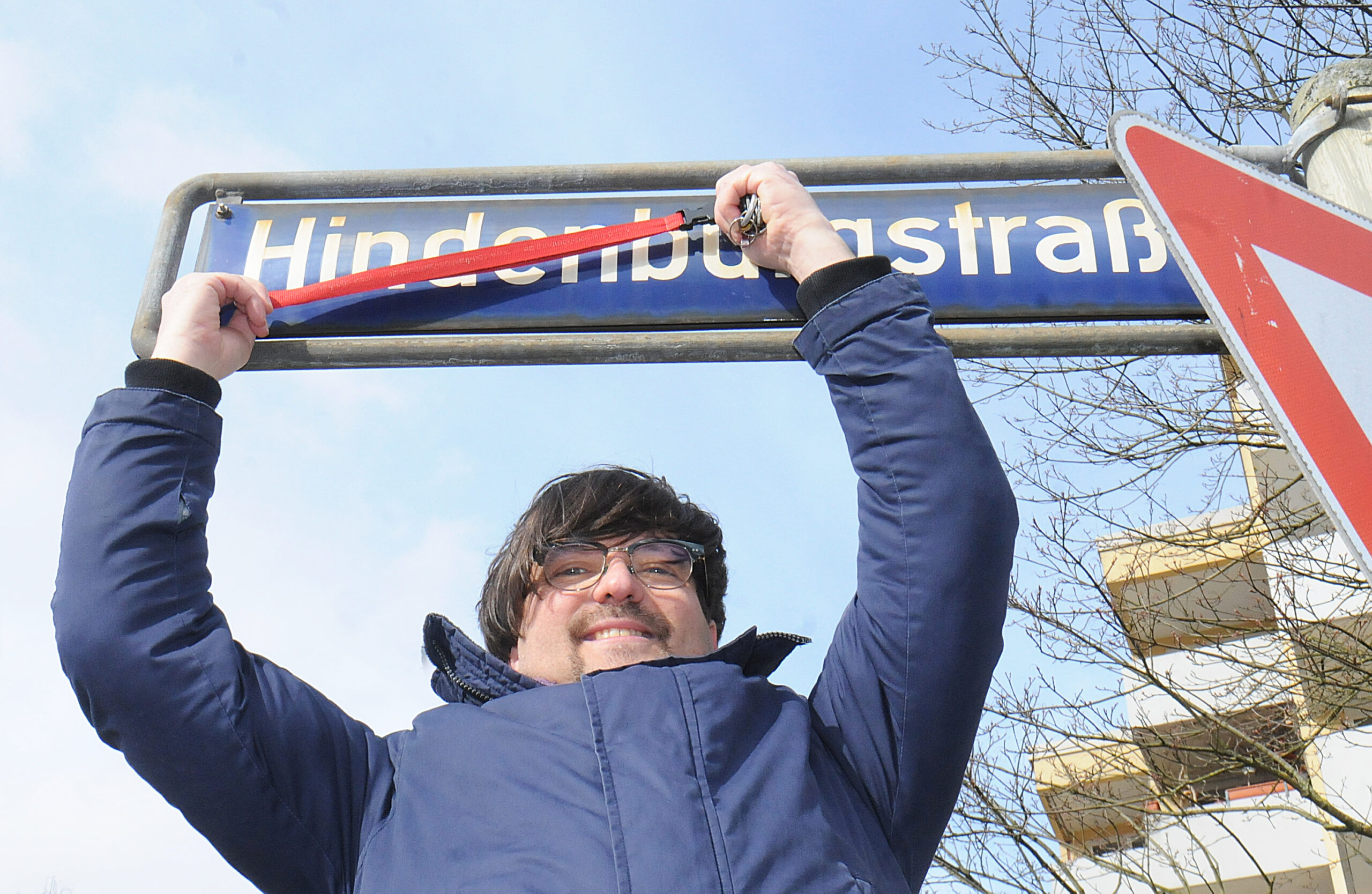 Rachid Messaoudi von den Linken in der Bezirksversammlung Nord streicht symbolisch den Namen Hindenburgstraße auf einem Straßenschild durch.
