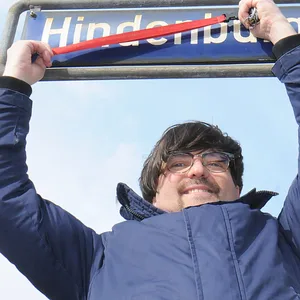 Rachid Messaoudi von den Linken in der Bezirksversammlung Nord streicht symbolisch den Namen Hindenburgstraße auf einem Straßenschild durch.