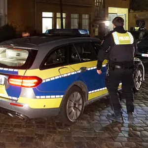 Ein Polizist steht neben einem Polizeiauto vor einem Haus in Hamburg-Barmbek