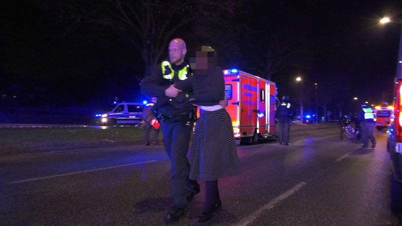 Ein Polizist geht in Alsterdorf mit einer Frau nach dem Amoklauf bei einer Veranstaltung der Zeugen Jehovas über die Straße