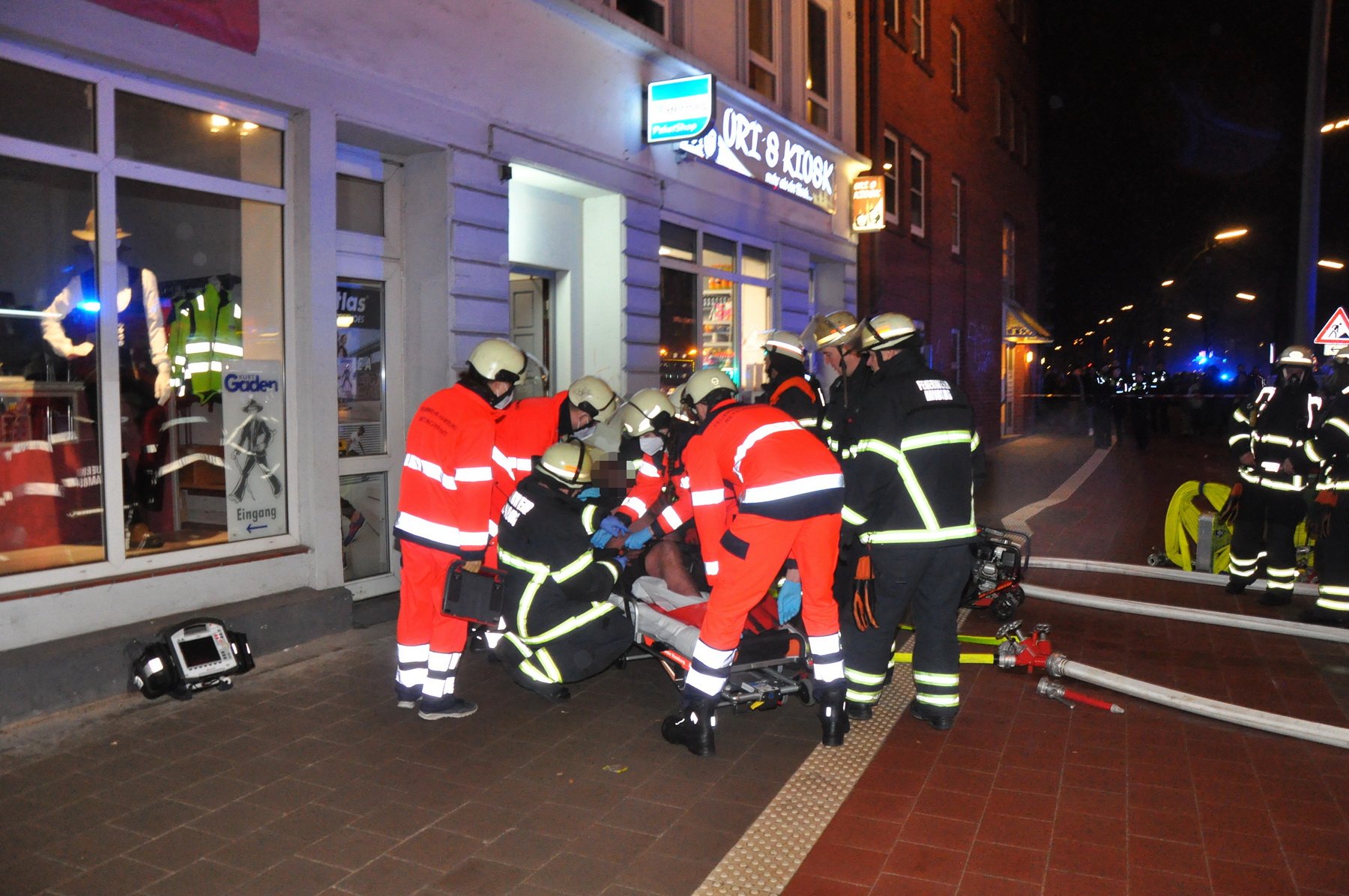 Rettungskräfte stehen auf dem Bürgersteig der Holstenstraße und versorgen einen Mann mit Brandverletzungen