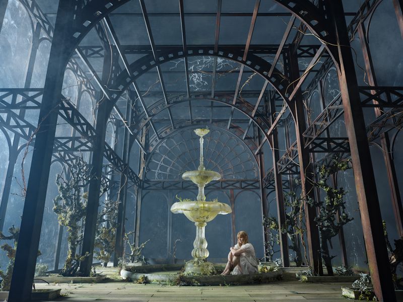 Eine Frau sitzt neben einem gläsernen Springbrunnen in einem Raum aus Eisenträgern im viktorianischen Baustiel