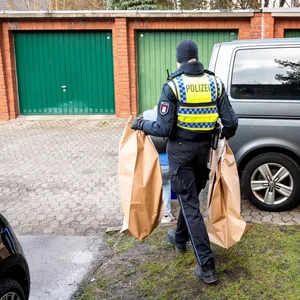 Eine Polizistin mit zwei braunen Säcken, in denen mutmaßliches Beweismittel ist.