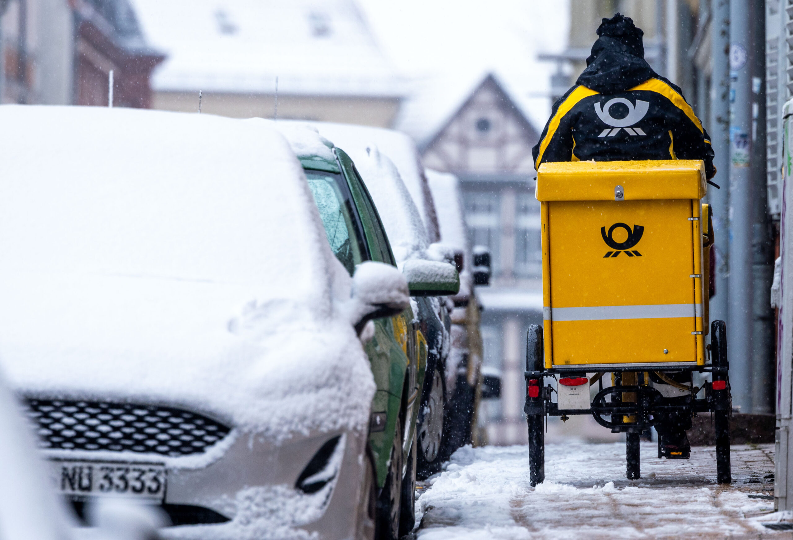 Eine Briefträgerin ist mit ihrem Fahrrad bei starkem Schneefall in der Altstadt von Schwerin unterwegs.