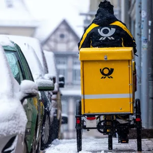 Eine Briefträgerin ist mit ihrem Fahrrad bei starkem Schneefall in der Altstadt von Schwerin unterwegs.