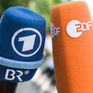 Fernsehmikrofone mit den Logos von ARD/BR und ZDF werden vor Beginn einer Pressekonferenz nebeneinander gehalten.