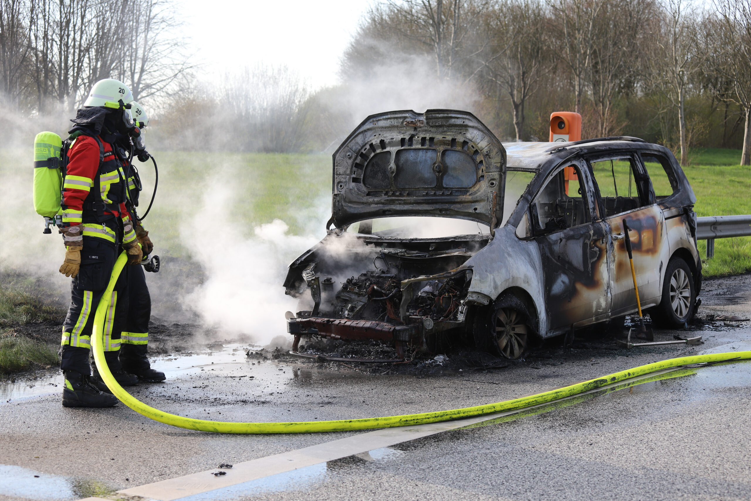 Zwei Feuerwehrleute stehen vor dem ausgebrannten Fahrzeug
