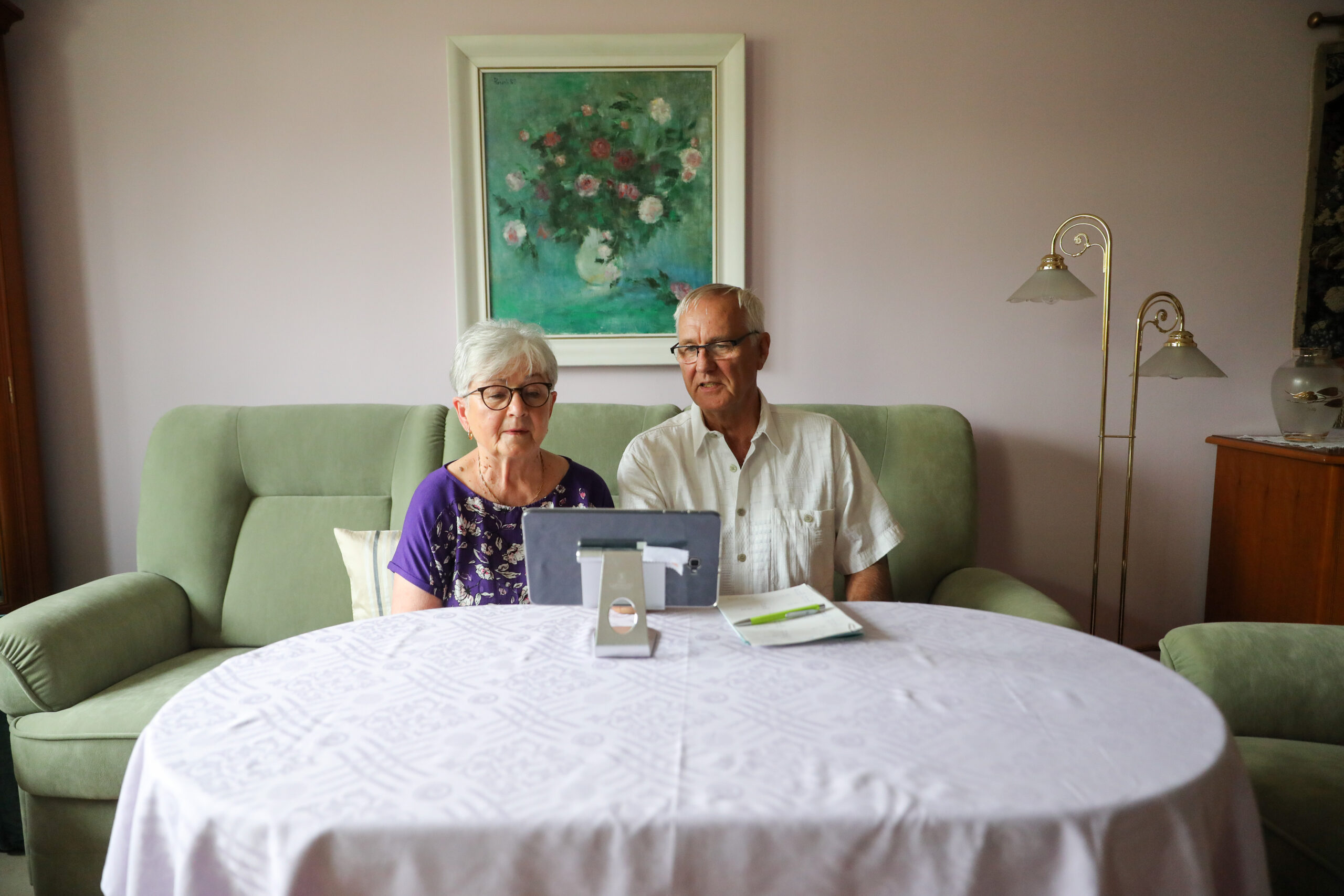 Ein Rentnerpaar sitzt in seinem Wohnzimmer vor einem Laptop