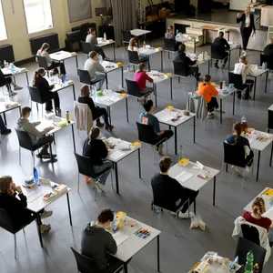 Schülerinnen und Schüler sitzen in einem großen Raum und schreiben eine Abiturprüfung. (Symbolbild)