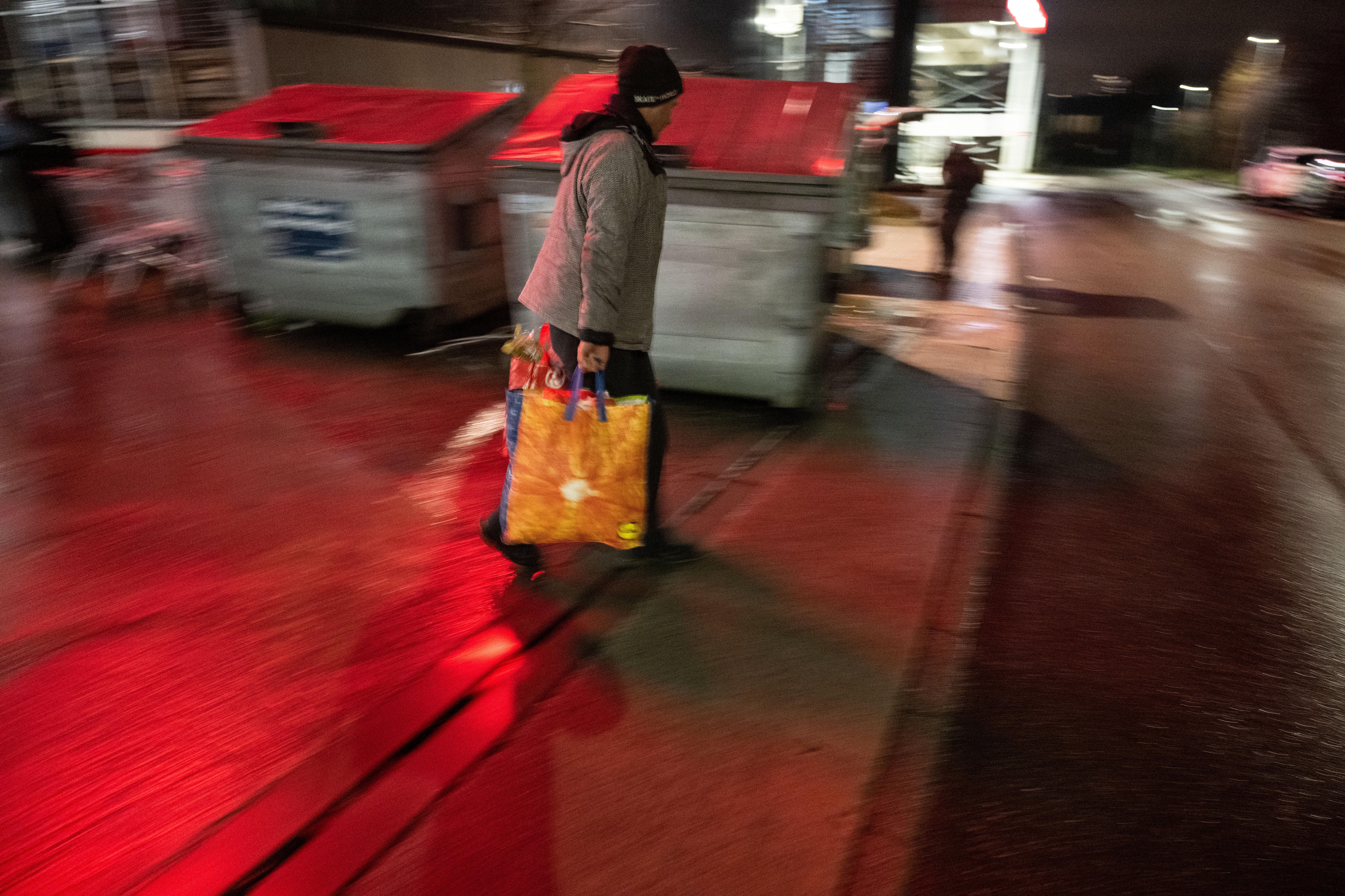 Ein Aktivist eht mit Taschen voller Lebensmittel an Containern eines Supermarktes vorbei.