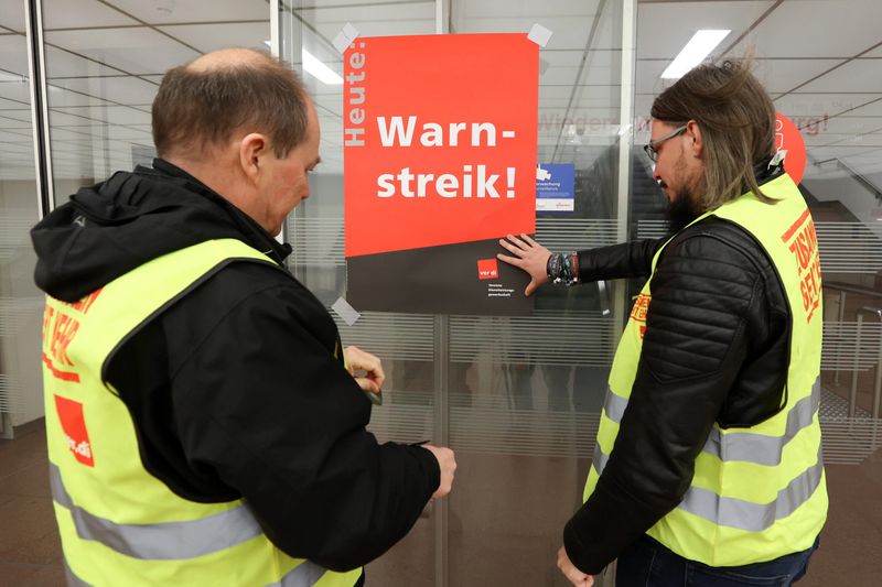 Gewerkschaftsvertreter kleben ein Plakat mit der Aufschrift «Warnstreik!» an eine Glastür am Flughafen Hamburg.