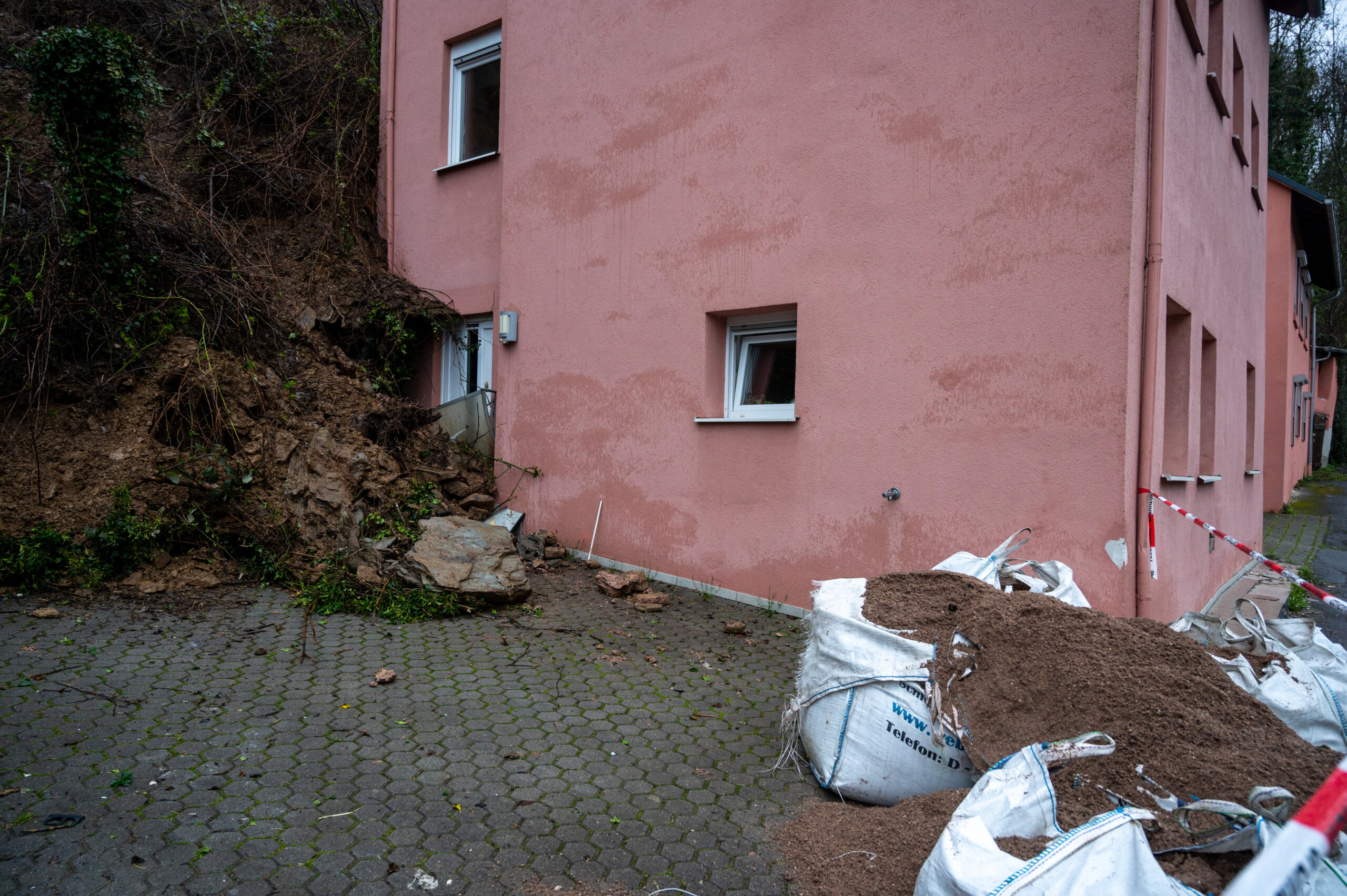 Ein rosanes Haus steht an einem Hang, Erde versperrt die Eingangstür.