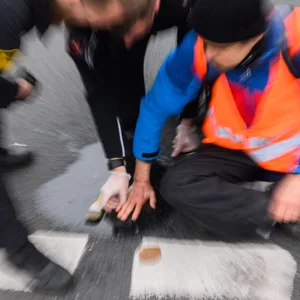 Polizisten versuchen festgeklebte Hände von Aktivisten der Gruppierung «Letzte Generation» am Deisterkreisel in Hannover mit Speiseöl von der Straße abzulösen.