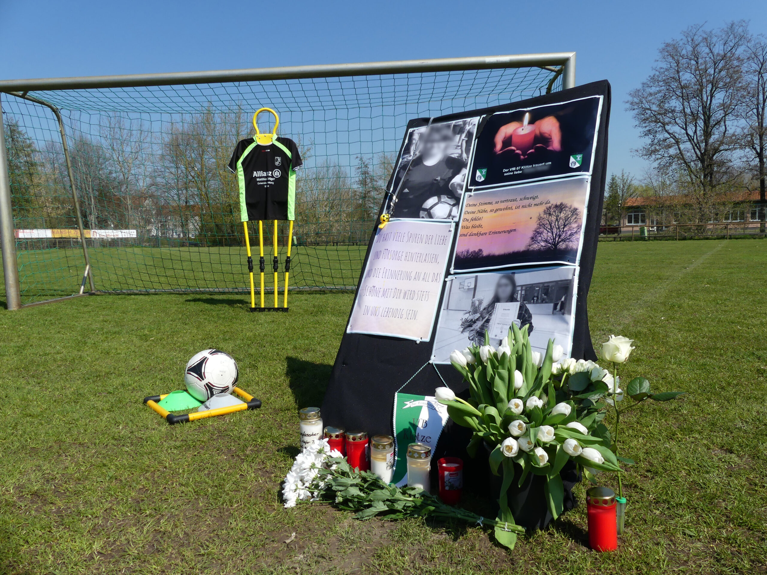 Bilder, Blumen und Kerzen stehen vor einem Fußballtor.