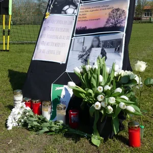 Bilder, Blumen und Kerzen stehen vor einem Fußballtor.